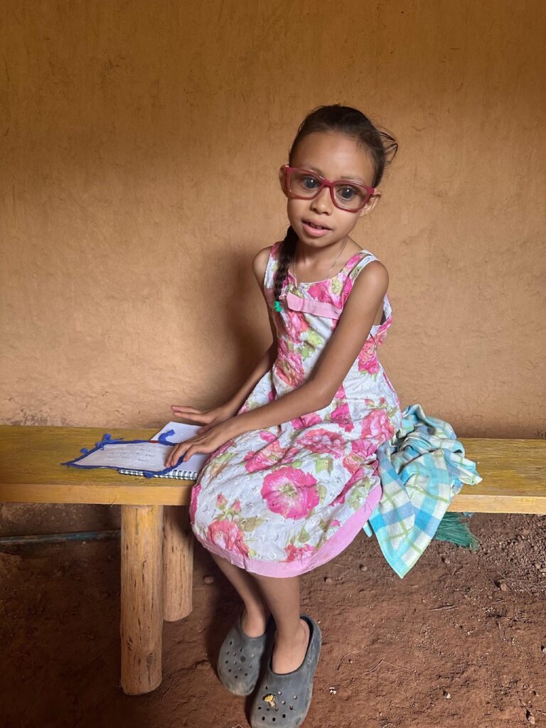 Partially sighted girl sits on a bench with her Braille beside her, learning to read it. She has glasses on to correct her vision.